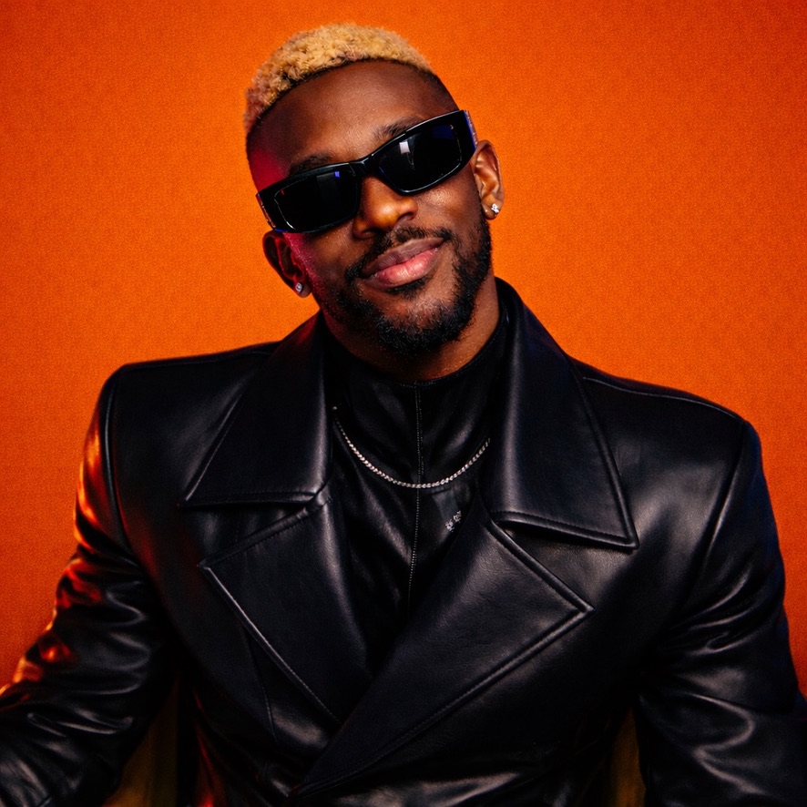 Marc Tovin smiling in sunglasses and black leather against a burnt-orange backdrop
